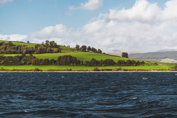 Zelené kopce poblíž řeky Firth of Clyde, panoramatický výhled z plachetnice. Dramatické nebe po bouři. Skotsko, Velká Británie. Cestovní destinace, ekoturistika, dovolená, čistá příroda. Atmosférická krajina - Fotografie, Obrázek