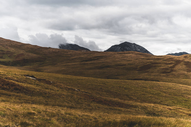Panoramiczny widok na dolinę w pobliżu najwyższego szczytu góry Paps of Jura (Beinn ir) pod zachmurzonym błękitnym niebem. Dramatyczne chmury. Wyspa Jura, Hebrydy Wewnętrzne, Szkocja, Wielka Brytania. Krajobraz atmosferyczny. - Zdjęcie, obraz