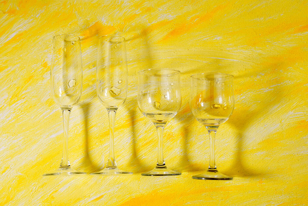 Variété de verres vides à boire sur fond jaune avec des ombres dures et des reflets du soleil. concept sobre. la vue du haut - Photo, image