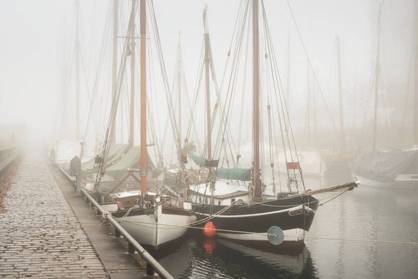 Elegáns és modern jachtok, vitorlás és halászhajók, kis hajók kikötve ti egy mólón egy sűrű köd. Látványosságok, városnézés, régi kikötő, történelem, múlt. Sepia-kép effektus. Germaniahafen, Kiel, Németország - Fotó, kép