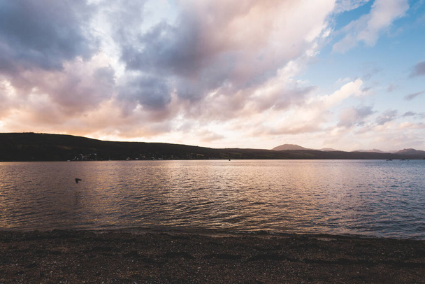 Η βραχώδης ακτή της λίμνης κάτω από τον θυελλώδη ουρανό μετά τη βροχή. Δραματικό σύννεφο ηλιοβασιλέματος. Gare Loch, Rhu, Σκωτία, Ηνωμένο Βασίλειο. Ταξιδιωτικοί προορισμοί, διακοπές, έννοιες δραστηριοτήτων αναψυχής - Φωτογραφία, εικόνα
