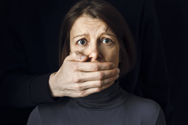 Bir kadına karşı şiddet kavramı. Adamın eli, kadının ağzını siyah arka planda kapatır.. - Fotoğraf, Görsel