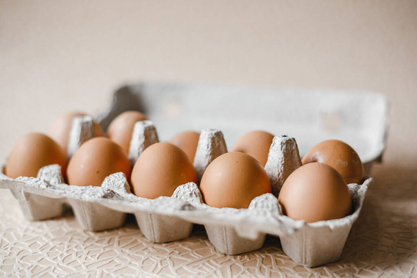 10 коричневих курячих яєць лежать у картонному лотку на столі
 - Фото, зображення