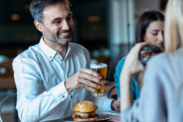 Aufnahme einer attraktiven Gruppe junger Freunde, die Burger essen, während sie reden und Spaß im Restaurant haben. - Foto, Bild
