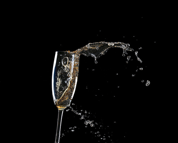 Glass of champagne with splash, on black background - 写真・画像