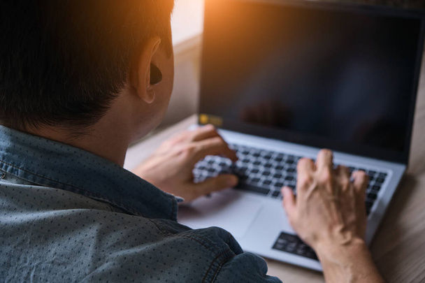 Zugeschnittenes Bild eines jungen Mannes, der zu Hause an seinem Laptop arbeitet, Hände, die mit Laptop auf dem Tisch beschäftigt sind, männliche Eingabe auf dem Computer - Foto, Bild