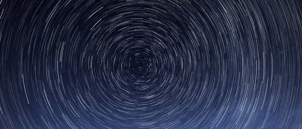 Αστρικά μονοπάτια, η περιστροφή των φωτεινών αστεριών τη νύχτα γύρω από το Πολικό Αστέρι ενάντια σε έναν γαλάζιο ουρανό και έναν μετεωρίτη - Φωτογραφία, εικόνα
