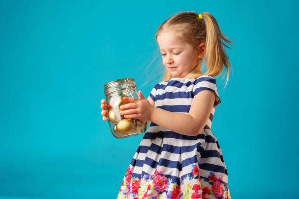 Blonde toddler girl with glass jar full of golden painted eggs for Easter - Zdjęcie, obraz
