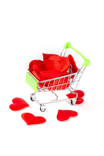 Игрушечная тележка из супермаркета, наполненная красными сердцами, изолированными на белом фоне, концепция любви и Дня Святого Валентина. - Фото, изображение