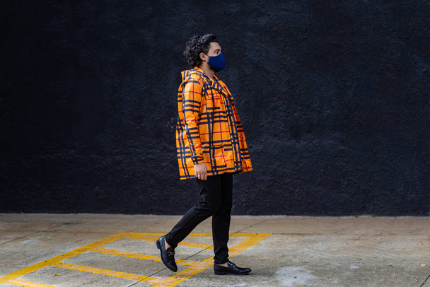 Young man on the street wearing a mask and wearing a yellow jacket and a black wall in the background. - 写真・画像