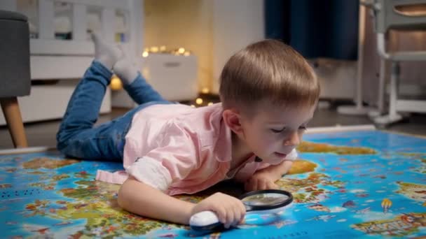 Gelukkige lachende jongen met vergrootglas op de grote wereldkaart. Concept van reizen, toerisme en onderwijs voor kinderen. Verkenning en ontdekkingen van kinderen. - Video