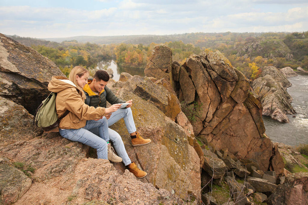 Couple of travelers with backpacks and map sitting on steep cliff. Autumn vacation - Fotografie, Obrázek