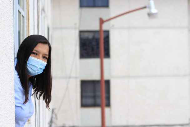 Латинська жінка з захистом маски клінічне використання ковалентних дивлячись у вікно - Фото, зображення