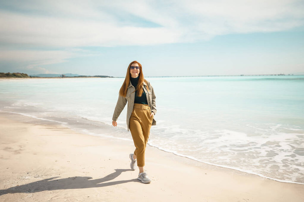 young beautiful red-haired girl walking on the beach near the ocean - Φωτογραφία, εικόνα