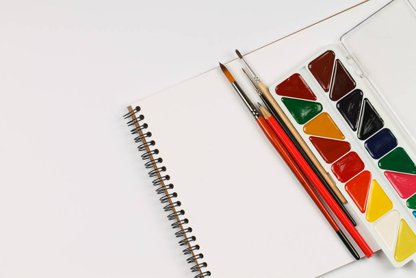 Ein Satz Aquarellfarben, Notizbuch und Pinsel auf einem weißen Tisch. Schöpfung. - Foto, Bild