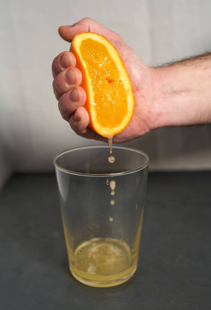 Male hand squeezing an orange into a glass. - Photo, Image