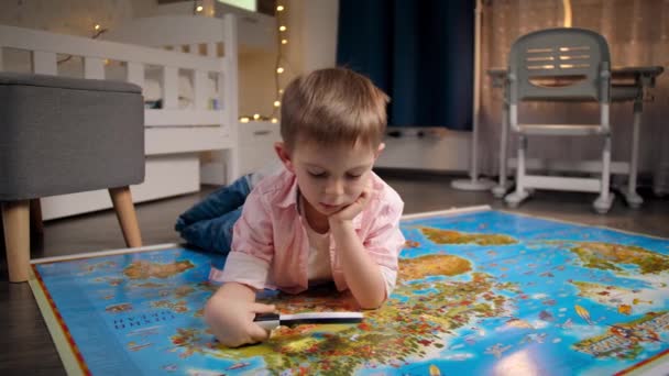 Dolly shot of little boy lying on floor at night and exploring big world map .Concept of travel, tourism and child education. Kids exploration and discoveries. - Footage, Video