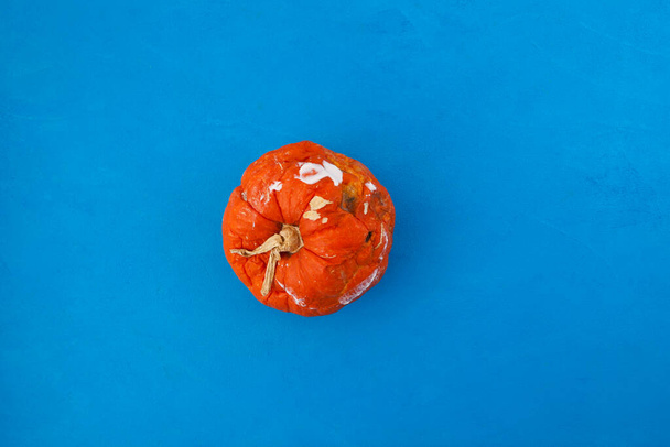 Rotten spoiled pumpkin on blue blotchy background. Ugly moldy vegetable. Top view, selective focus. Improper food storage. Concept - reduction of organic waste. - Photo, Image