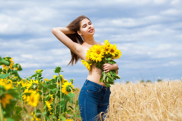 Portrait of a half-naked girl with a bouquet of sunflowers posing on a field background - Фото, зображення