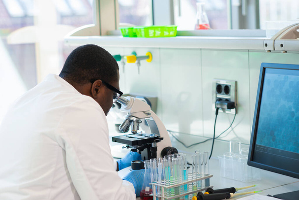 African-american man working in lab. Scientist doctor making medical research. Laboratory tools: microscope, test tubes, equipment. Biotechnology, chemistry, science, experiments and healthcare. - Φωτογραφία, εικόνα
