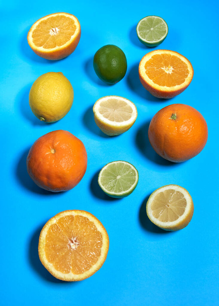 Naranjas enteras y partidas, limas y limones con piel sobre fondo azul. CITRUS CITRIC - Foto, imagen