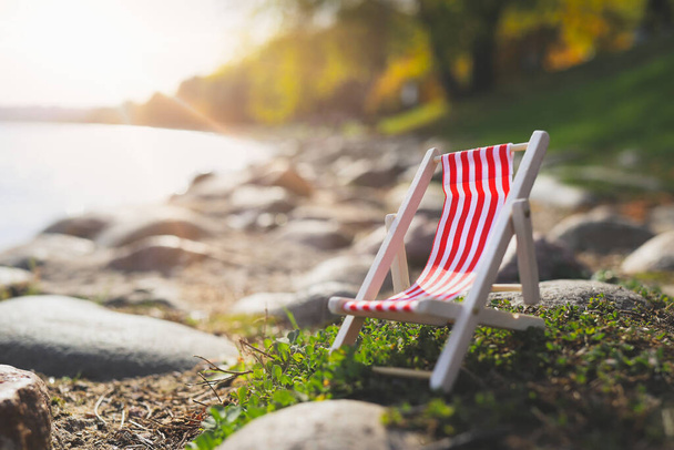 red empty striped chaise longue on rocks by lake. - 写真・画像