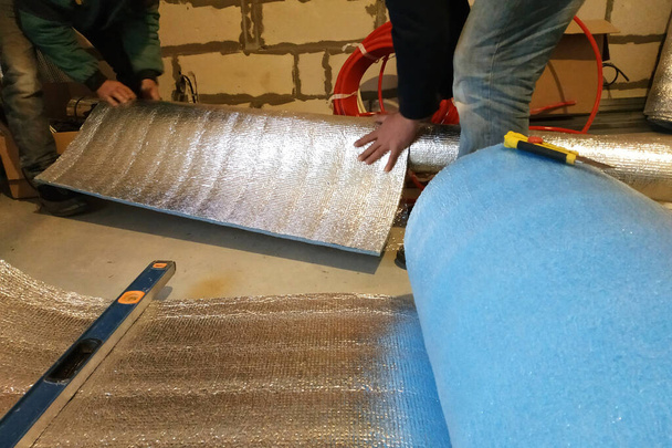 εργάτες τυλίγουν γαλβανισμένο σωλήνα με αλουμινόχαρτο στο νεόδμητο σπίτι. Μετρήστε το μήκος και το πλάτος του φύλλου, τυλίξτε το και κολλήστε το. 2020 - Φωτογραφία, εικόνα