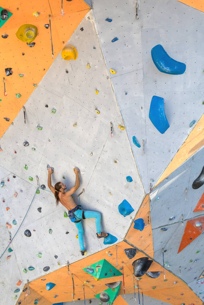 Un hombre trepa un muro de escalada, un escalador está entrenando en terreno artificial, escalada en roca en la ciudad, un hombre fuerte, deportes en la ciudad, seguridad en deportes extremos. - Foto, imagen