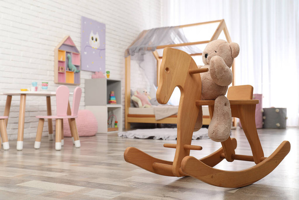 Teddy bear on wooden rocking horse in child's room, space for text. Interior design - Φωτογραφία, εικόνα