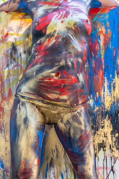 Μια γυμνή γυναίκα ζωγραφίζεται με πολύχρωμη μπογιά σε ένα περιβάλλον σπιτιού. - Φωτογραφία, εικόνα