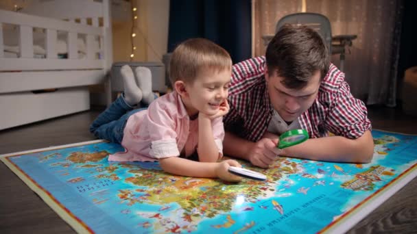 Glücklich lächelnder kleiner Junge mit jungem Vater, der die Weltkarte erkundet und zusammen Spaß hat. Konzept für Reisen, Tourismus und Kindererziehung. Kinder erkunden und entdecken - Filmmaterial, Video