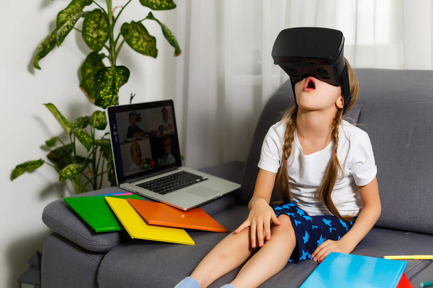 Trying new technologies. Little schoolgirl wearing big VR glasses being impressed playing virtual games. Home school, online education, home education, quarantine concept - Image - Zdjęcie, obraz