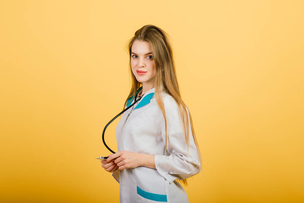 Friendly female doctor smiling - isolated over yellow background, studio - Fotó, kép