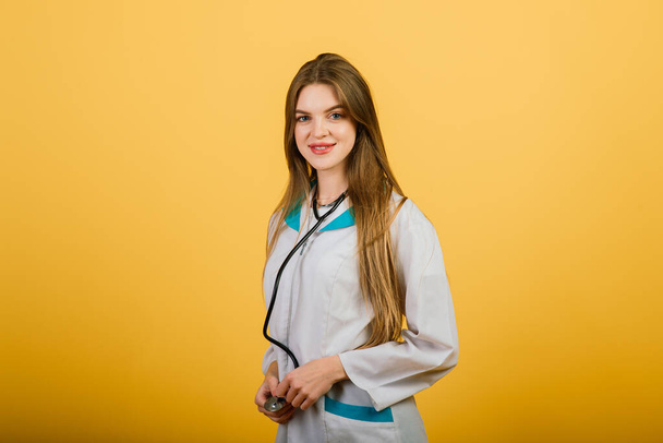 Vriendelijke vrouwelijke arts glimlachen - geïsoleerd over gele achtergrond, studio - Foto, afbeelding