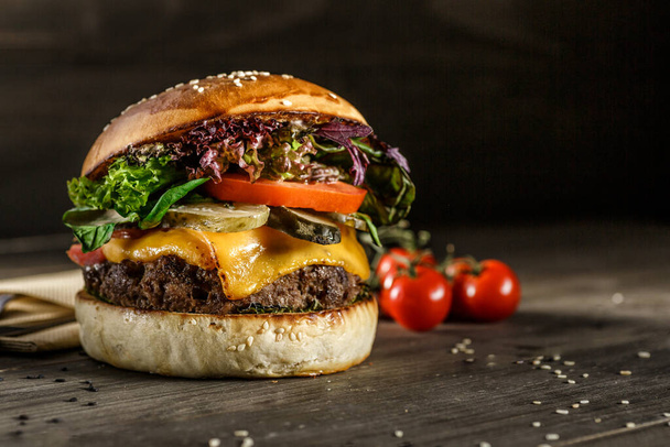 Closeup photo of home made fresh burger with beef, onion, tomato, lettuce, cheese and spices.burger on the board on a dark background - Foto, immagini