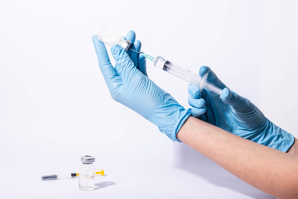 COVID-19 vaccin, arts, onderzoeker houdt handen spuit in blauwe handschoen met griep, mazelen, rubella of hpv vaccin en spuit met naald vaccinatie voor baby, kind, vrouw of man neergeschoten. - Foto, afbeelding