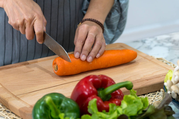 Gros plan de la carotte main femme avec couteau de cuisine sur la planche à découper. Chef coupe les légumes en un repas.  - Photo, image