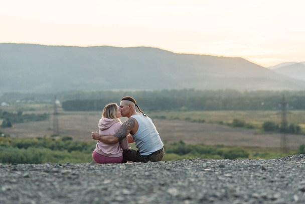 Young man hugs his girlfriend on the mountain peak at sunset background. - Foto, afbeelding