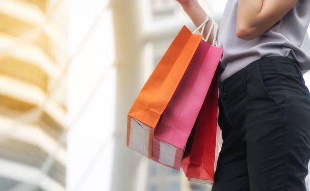 女性の都市の背景にショッピングバッグを運ぶ手。幸福や消費主義販売や人々の概念は. - 写真・画像