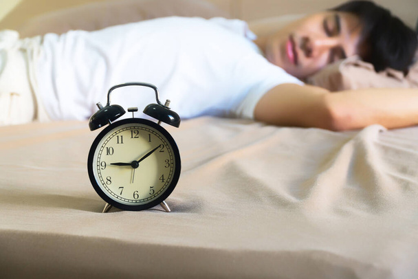 Yakışıklı bir adamın yatakta uyuduğu çekici siyah çalar saat. O, işten geç saatlere kadar yorgundu.. - Fotoğraf, Görsel