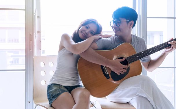 Happy couple entertainment concept. Young man playing guitar for his girlfriend listening at home together. - Photo, Image