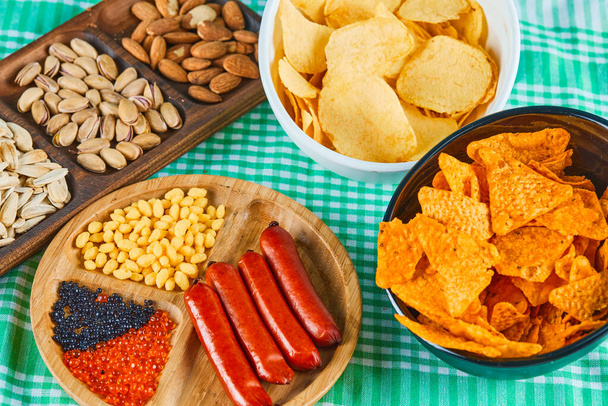 Diverse snacks, schaal chips en een bord worstjes op een blauwe tafel - Foto, afbeelding