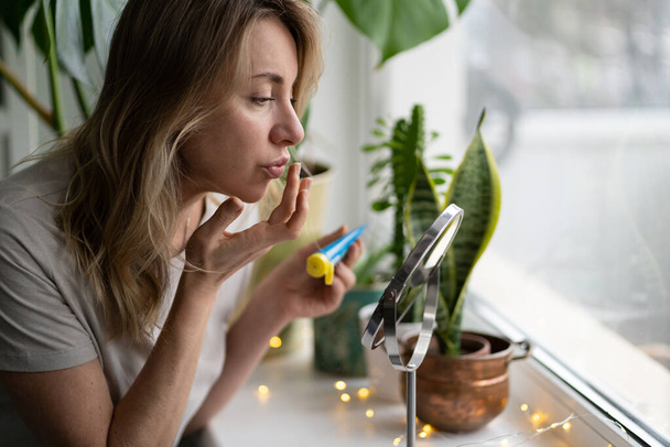 Woman applying moisturizing nourishing balm to her lips with finger to prevent dryness and chapping - Photo, Image