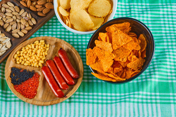 Verschiedene Snacks, eine Schüssel Pommes und ein Teller Würstchen auf einem blauen Tisch - Foto, Bild