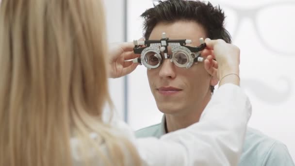 Sopra la spalla vista di oftalmologo femminile caucasico esaminando la vista del paziente maschile mettendo speciale strumento oftalmologico su di lui - Filmati, video