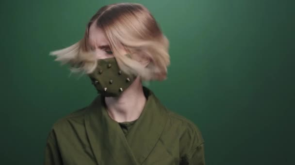 Portrét se zpomalením silné mladé ženy v ozdobené obličejové masce pózující na zeleném pozadí - Záběry, video
