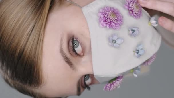 Вертикальный экстрим женщины-модели в маске, украшенной цветами, смотрящей на камеру и позирующей - Кадры, видео
