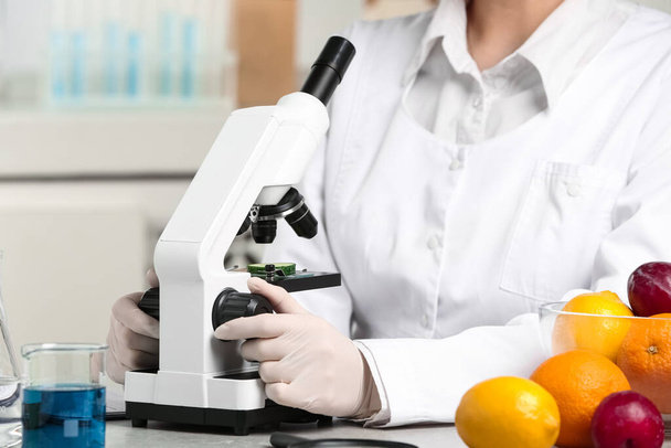 Scientist inspecting slice of cucumber with microscope in laboratory, closeup. Poison detection - Foto, Imagen