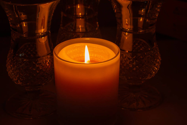輝く黄金のろうそくの炎のマクロ抽象的な焦点を当てたビューは、暗いテーブルの上に近くのヴィンテージの鉛ガラス製品を照らす - 写真・画像