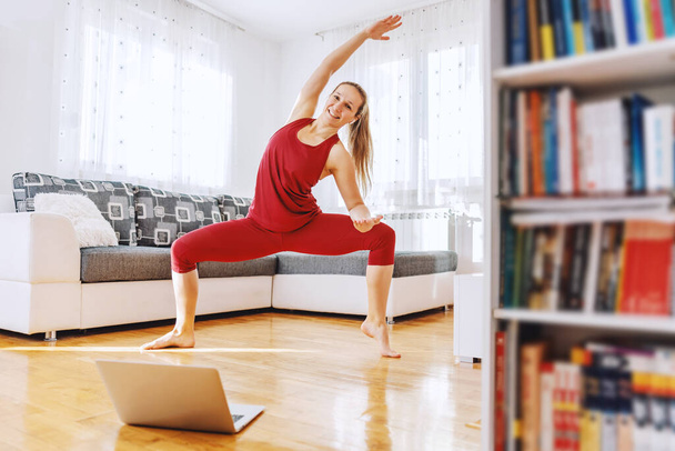 Gülümseyen formda yoga hocası Tanrıça yoga poziyonunda duruyor ve internetten ders alıyor. İç mimari. - Fotoğraf, Görsel